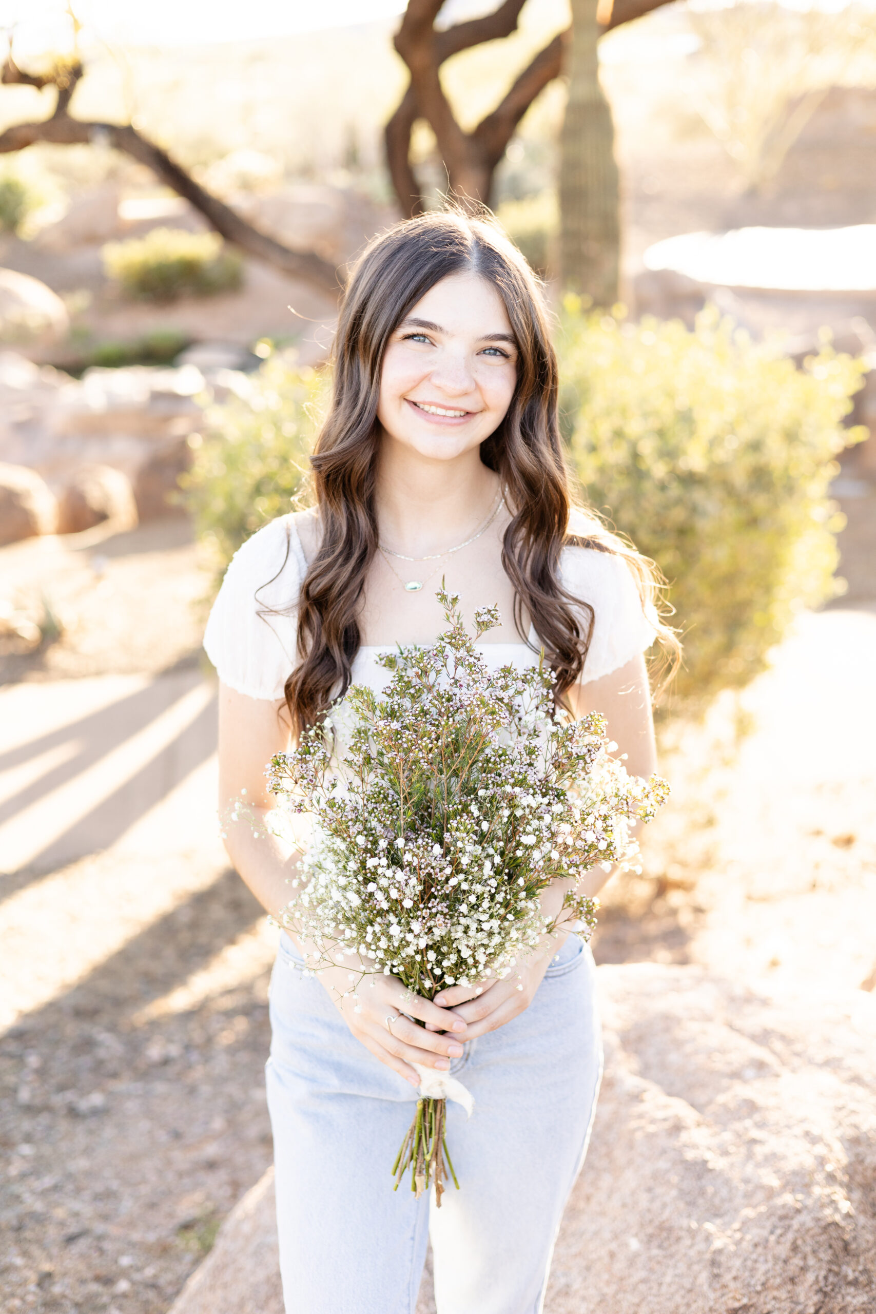 Peoria, AZ senior girl holding bouquet of flowers in white top and denim jeans for senior photography session.