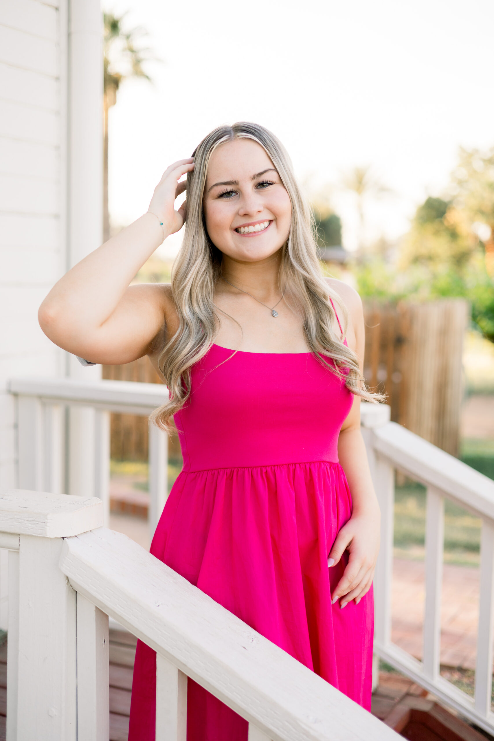 Senior in pink dress stands on the stairway of historic building at Sahuaro Ranch Park.