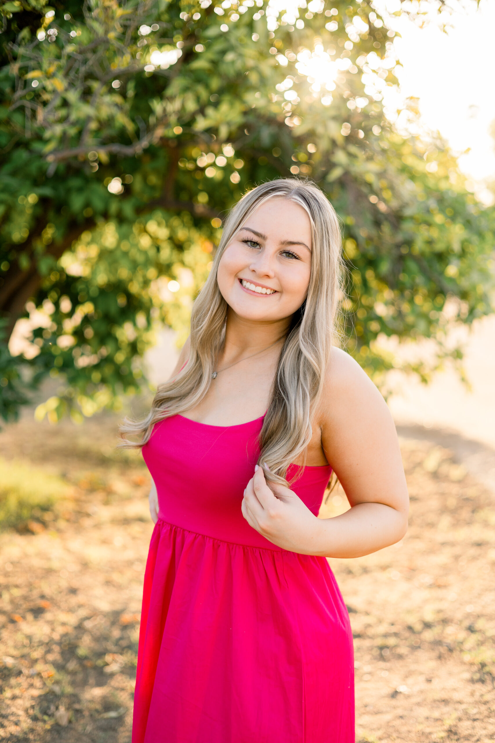 Senior in pink dress stands among citrus grove in Glendale, AZ.