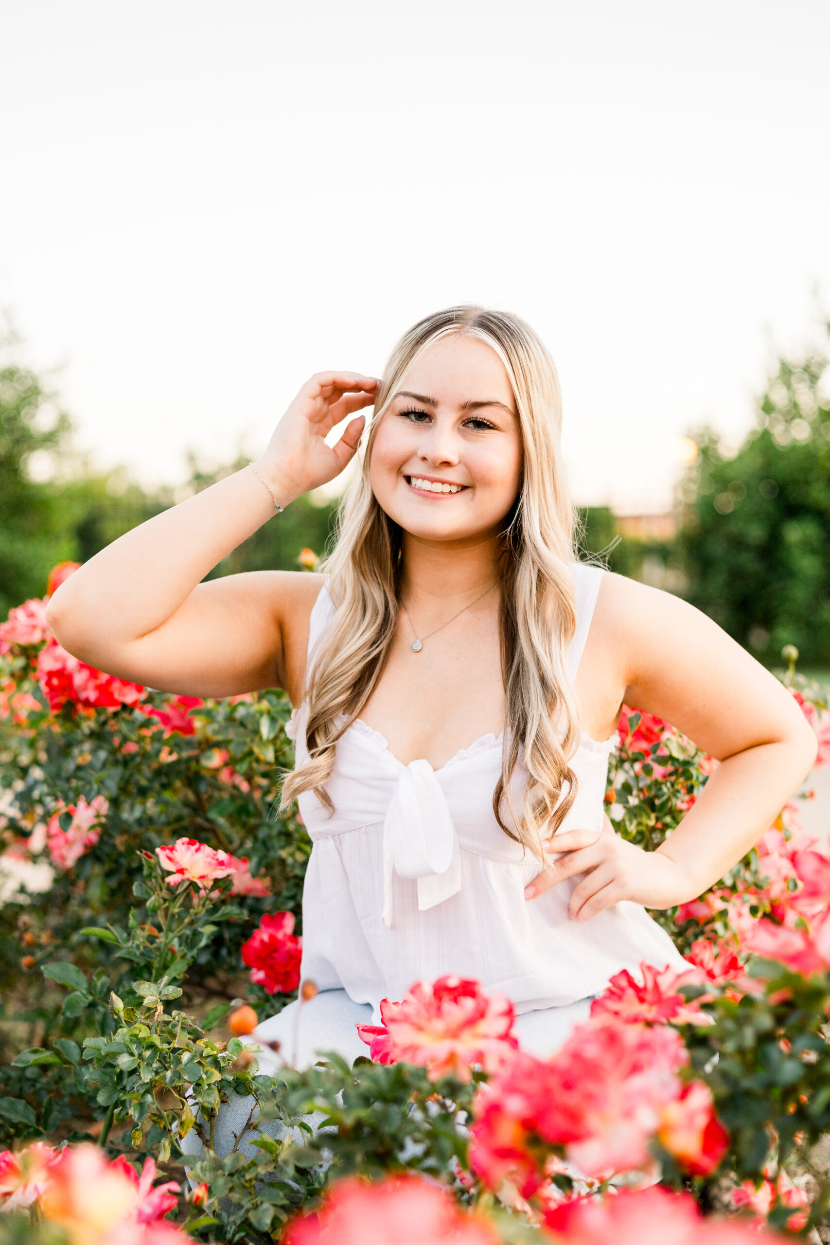 Senior poses among pink roses in rose garden.